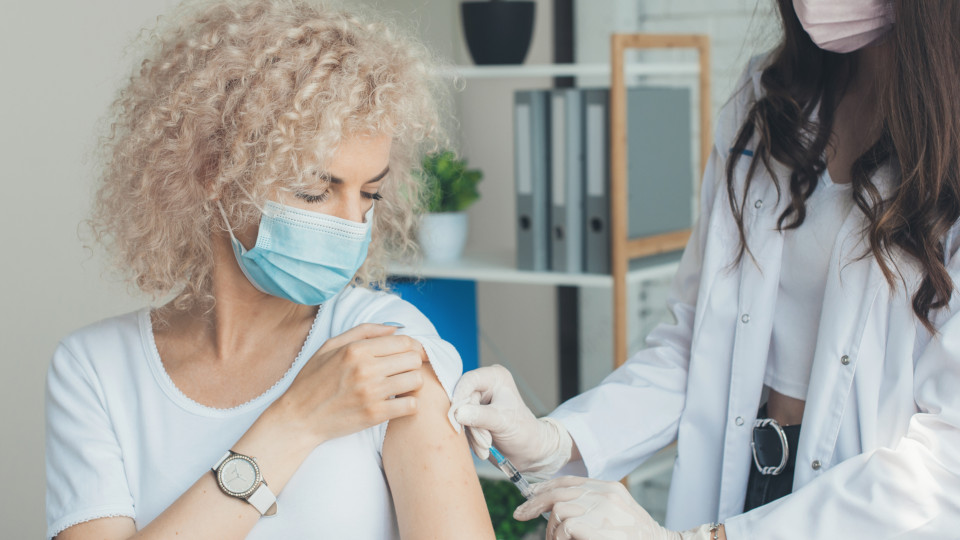 Blonde Frau mit Locken, die gerade von einer Ärztin ihre Corona-Impfung erhält.