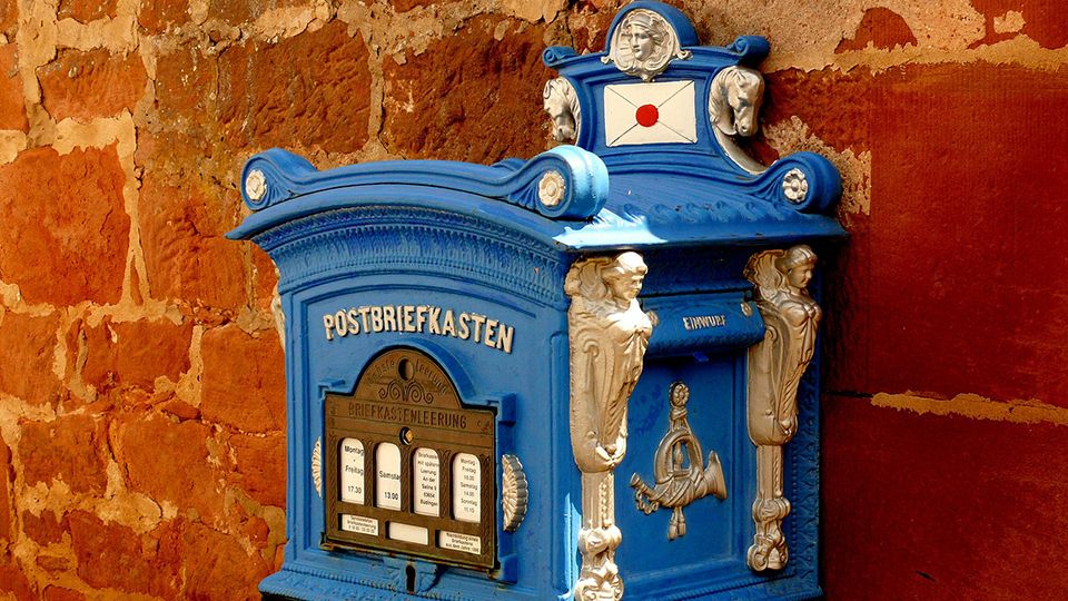 Blau-weißer antiker Briefkasten an einer roten Steinmauer.