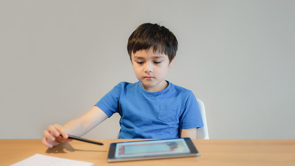 Digitale Kita: Junge, der gerae auf einem Tablet etwas nachschaut und lernt.