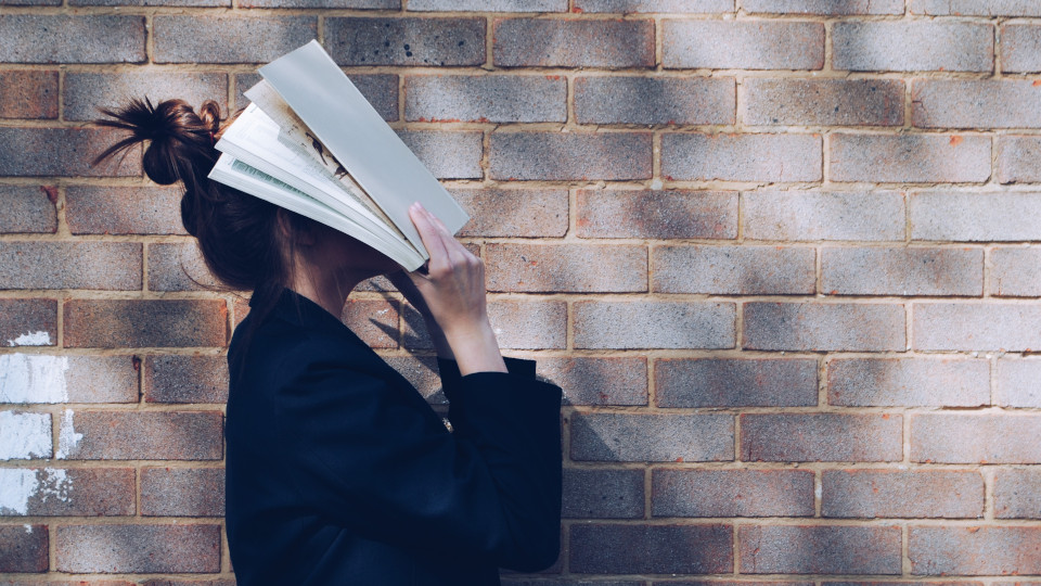 Frau bedeckt ihr Gesicht frustriert mit einem Buch