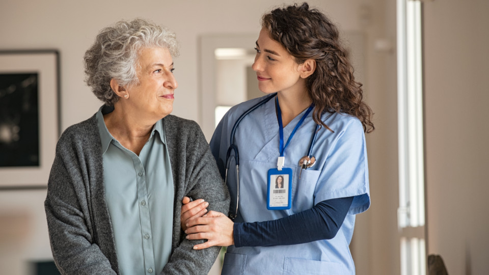 Pflegeberuf: Pflegekraft, die gerade eine Patientin beim Gehen unterstützt, beide lächeln.