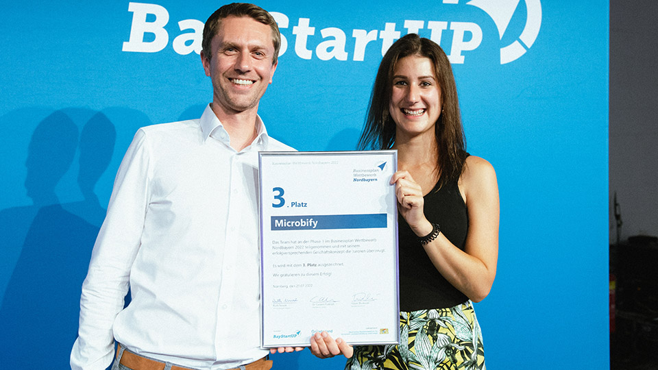 Dr. Georg Schmid und Linda Dengler nehmen die Urkunde für den dritten Platz beim BayStartUP-Businessplan Wettbewerb Nordbayern 2022 entgegen. 