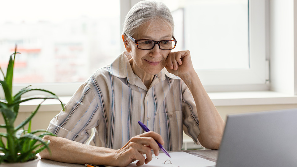 Kostenfreie PC-Kurse: Seniorin, die gerade am Laptop sitzt und sich etwas notiert.