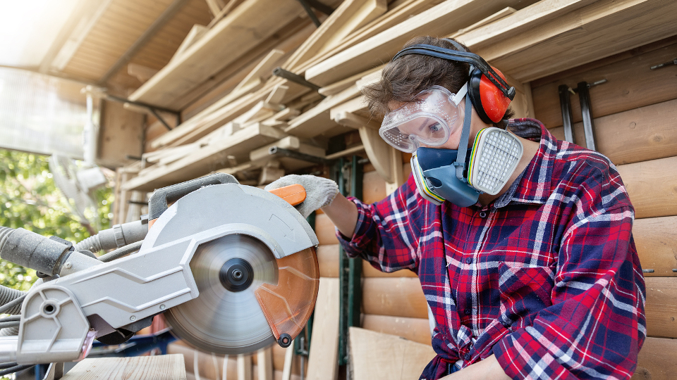 Young beautiful handy professional happy female strong carpenter portrait wearing protective goggles working in carpentry diy workshop with circular saw. Confident Women male hobby at workbench