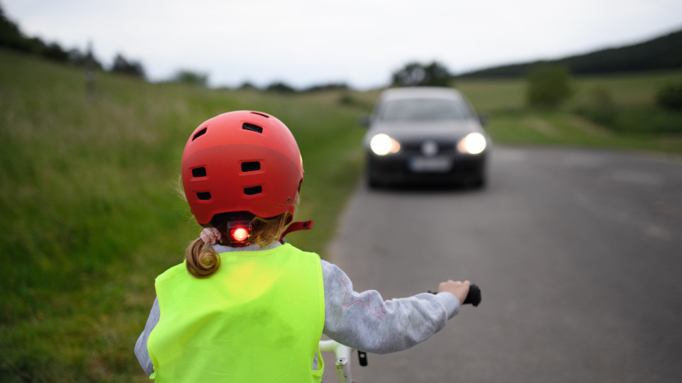 Verkehrssicherheit: Mädchen mit Helm und Warnweste und ein Pkw mit eingeschaltetem Licht.
