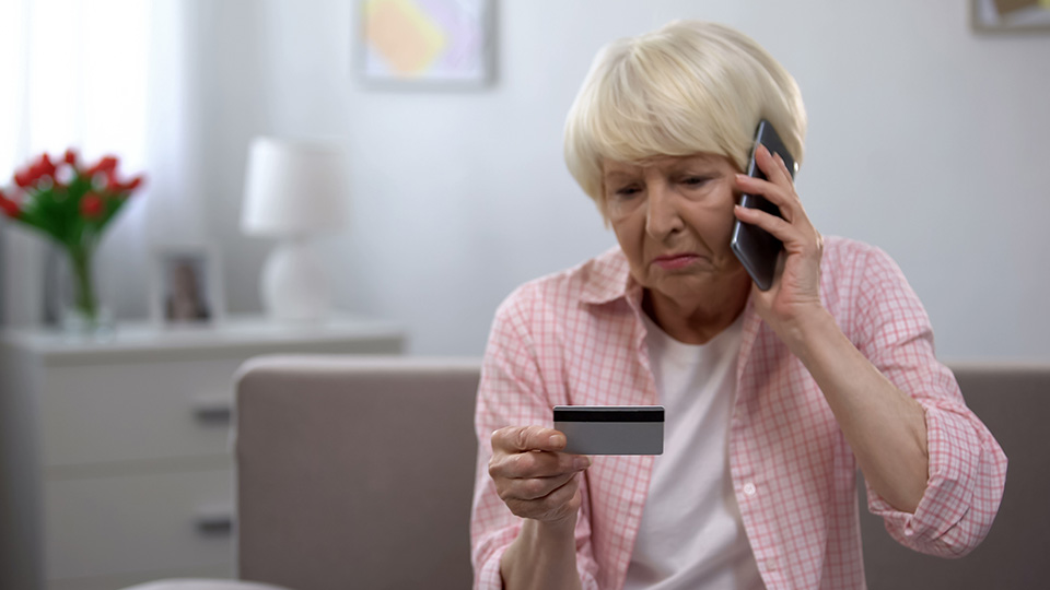 Kinder schützen Großeltern: Ältere Frau, die gerade einen Anruf bekommt und ihre Bankkarte betrachtet.