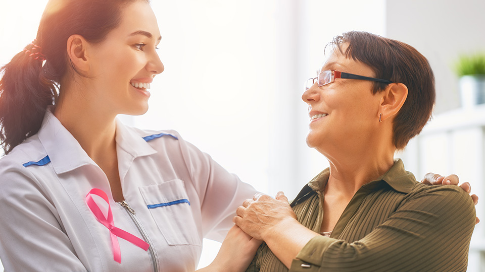Therapien und Heilungschancen bei Brustkrebs: Ärztin, die erkrankte Frau anlächelt und Arm über die Schulter legt.