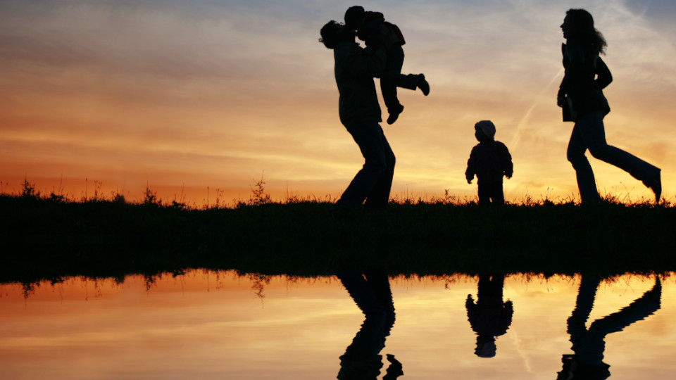 Thema Kindergeld als Inflationsausgleich: Familie mit zwei Kindern im Sonnenuntergang vor einem Gewässer.