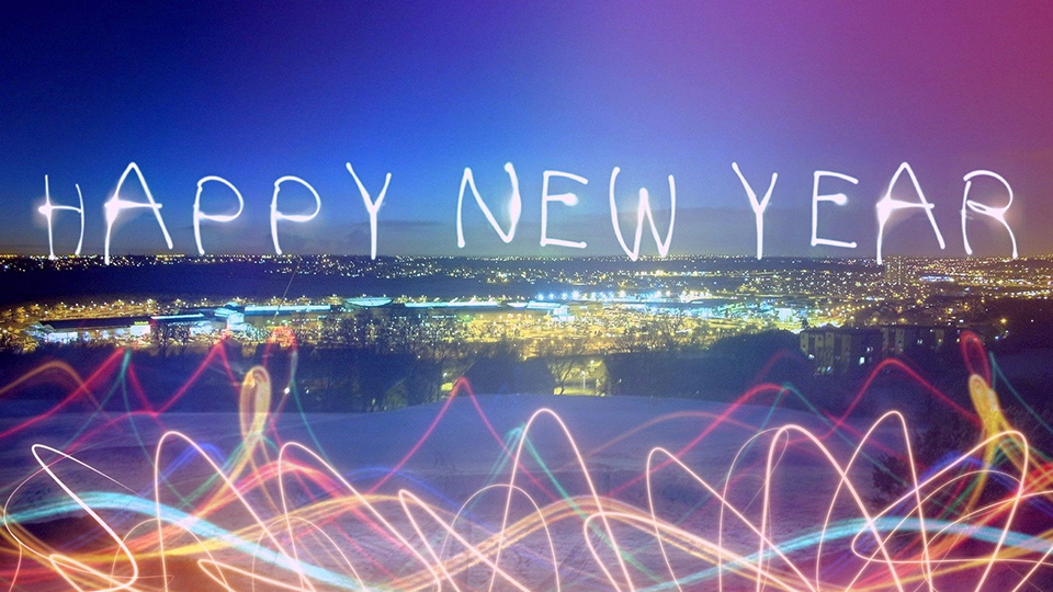 Silvesterparty: Schriftzug mit "HAPPY NEW YEAR" hinter einer bunten Reflexion und einer Aussicht auf eine Stadt.