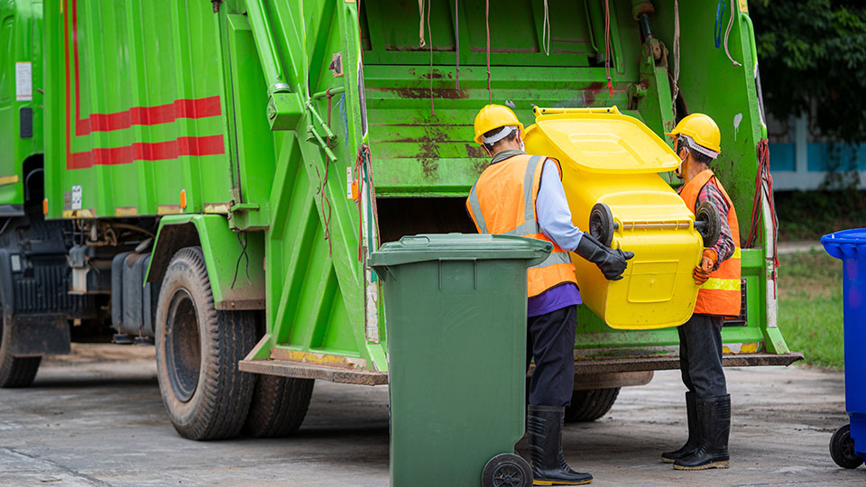 Gelbe Tonne, die gerade von zwei Männern in ein Fahrzeug der Müllabfuhr entladen wird.