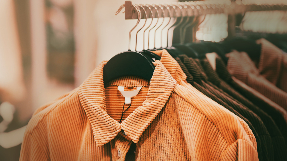 Beautiful corduroy coats for the autumn season in ginger and brown colors hang on hangers in a clothing store in the mall. Shopping.