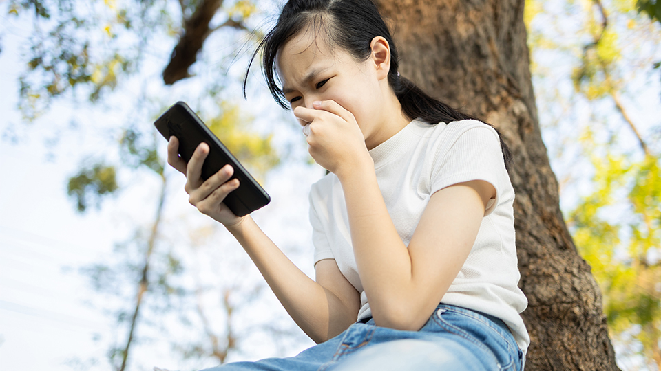 Cyber-Mobbing: Mädchen, das auf ihr Handy sieht und sich die Hand vor den Mund hält