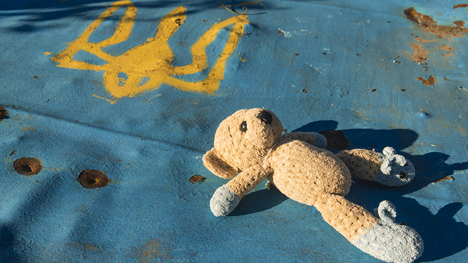 Ukraine-Krieg: Teddy liegt auf einer kaputten Fläche, auf der das Wappen der Ukraine zu sehen ist