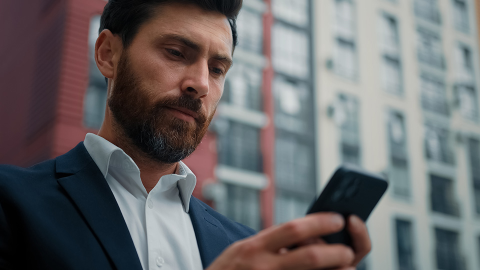 Arbeitszeiterfassung im 21. Jahrhundert: Mann steht vor Gebäude und gibt etwas ins Handy ein
