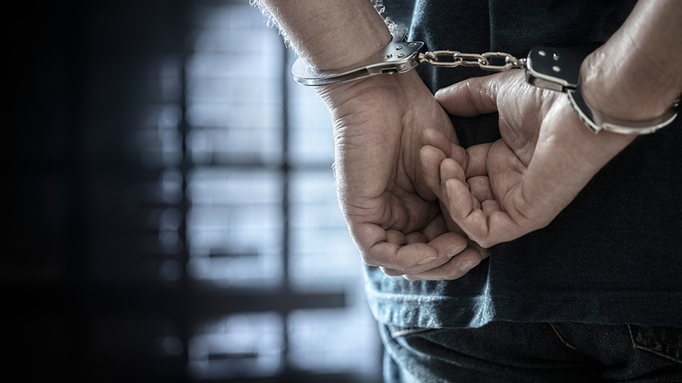 Mann festgenommen: steht in Handschellen vor Gitterstäben im Gefängnis
