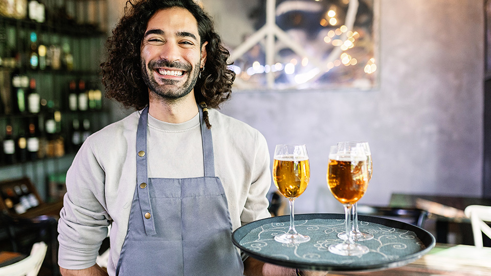 Gastro-Beschäftigter, der ein Tablett mit Weingläsern hält und glücklich in die Kamera lächelt