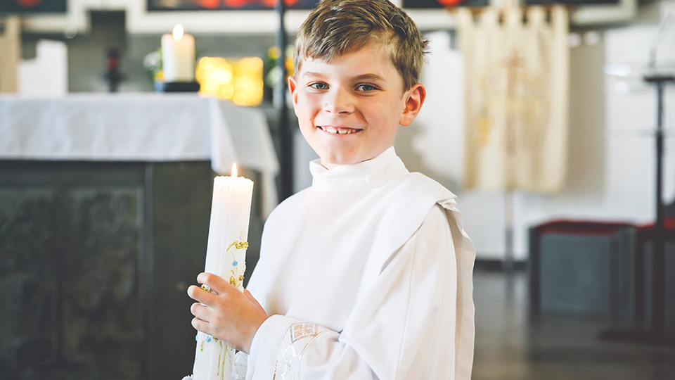Kommunion: Lächelnder Junge mit Kerze bei der Erstkommunion