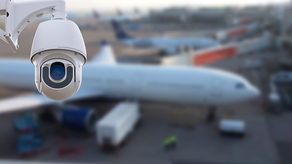 Gefahrenabwehr am Flughafen: Kamera im Vordergrund, im Hintergrund ein Flugzeug