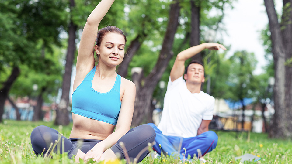 Sommer-Programm: Zwei Personen, die gerade Yoga im Park machen.