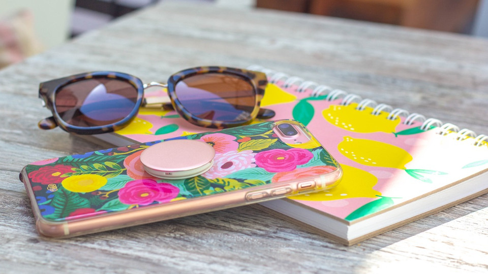 Bunte Handyhülle, die vor Sonnenbrille und buntem Notizbuch auf einem Tisch liegt