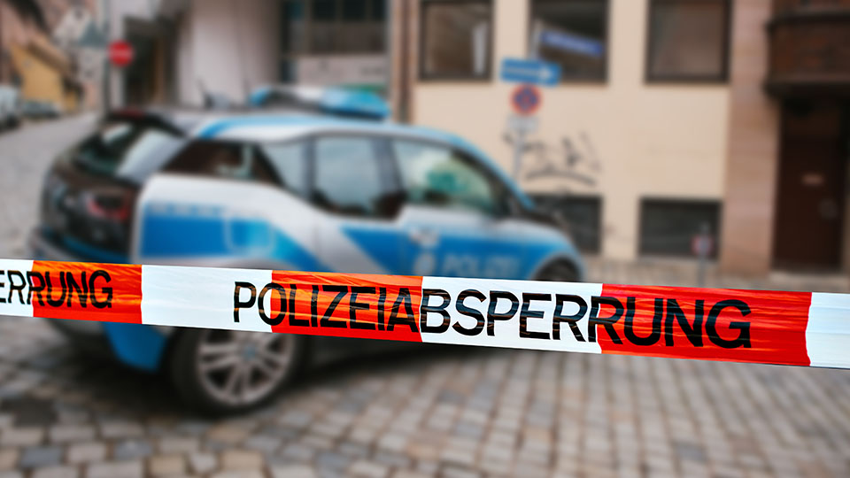 Streifenwagen der Polizei steht vor Gebäude hinter Absperrband der Polizei