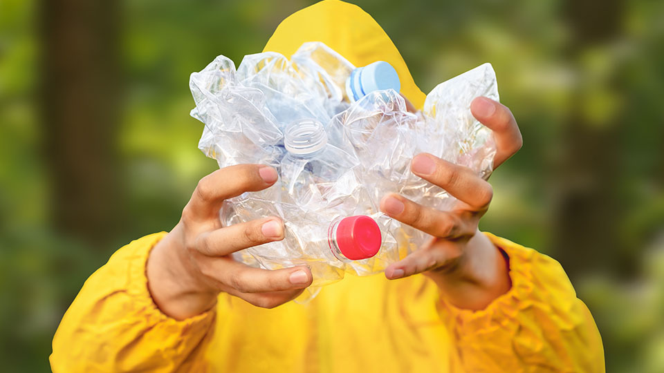 Aus dem Wasser gezogene Plastikflaschen in den Händen eines Mannes mit gelber Regenjacke