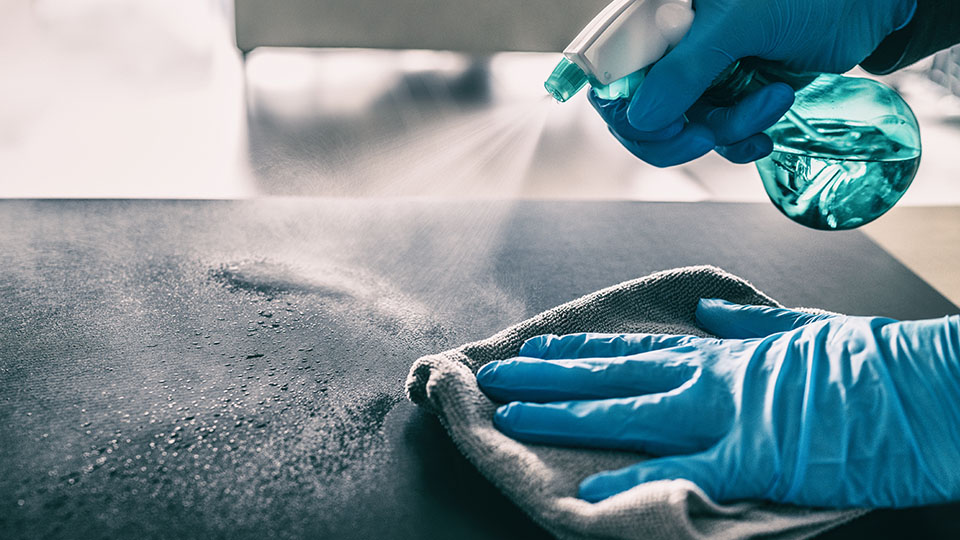 Hygiene in Krankenhaus und anderen Gesundheitseinrichtungen: Desinfektion von Fläche mit Desinfektionsspray und blauen Handschuhen