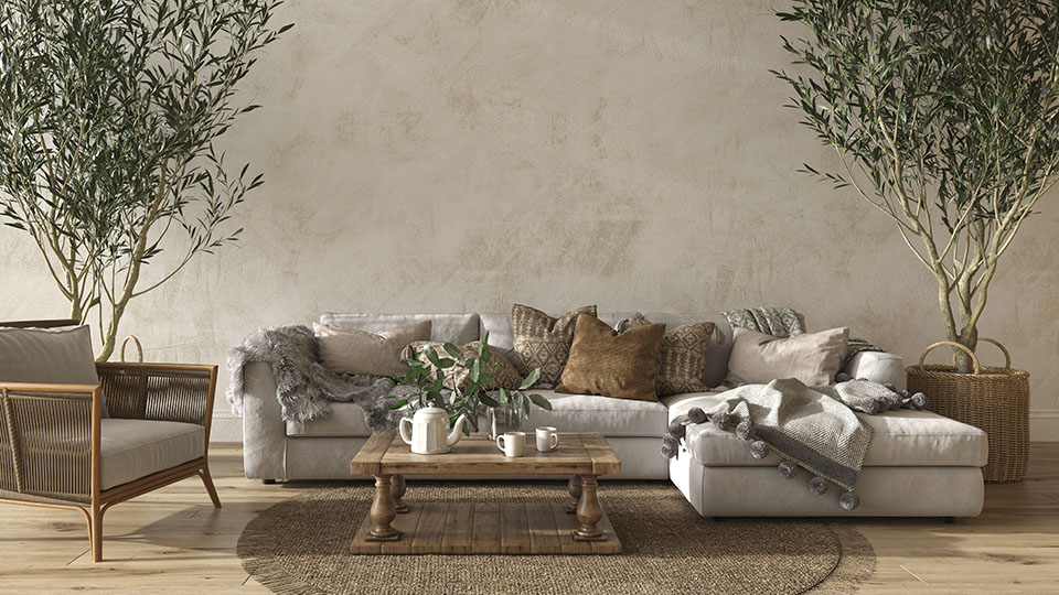 XXXLutz Must-Haves im Landhausstil: Hier eine beige Couch inmitten von zwei Pflanzen und viele Naturmaterialien