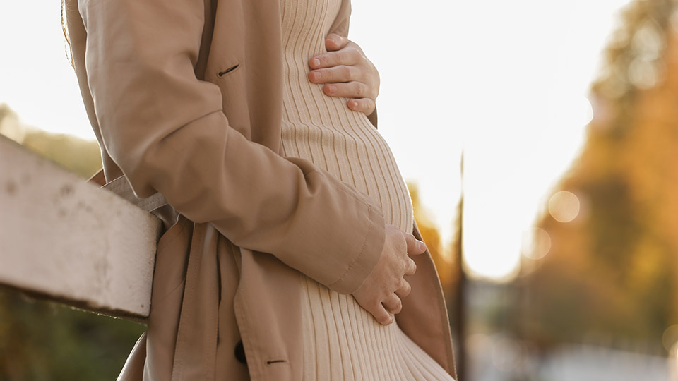 Schwangere Frau im beigen Strickkleid vor Herbstlandschaft