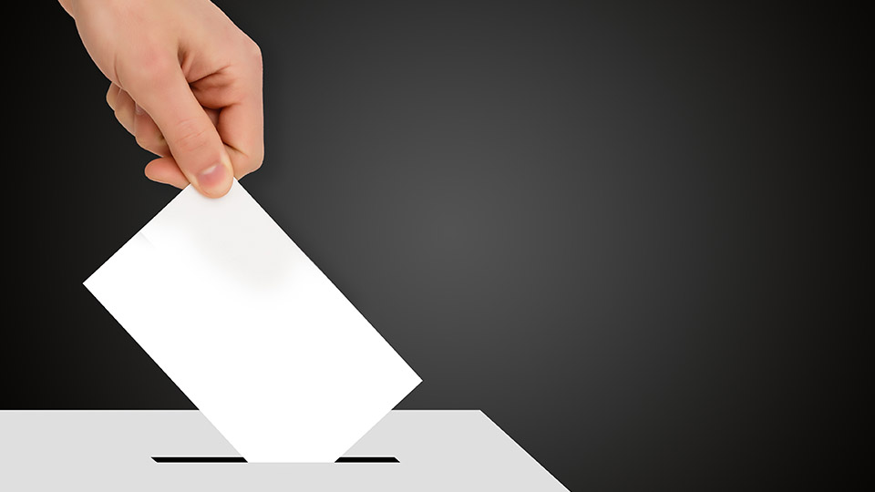 Landtagswahl 2023: Hand, die gerade Stimmzettel in die Wahlurne wirft.