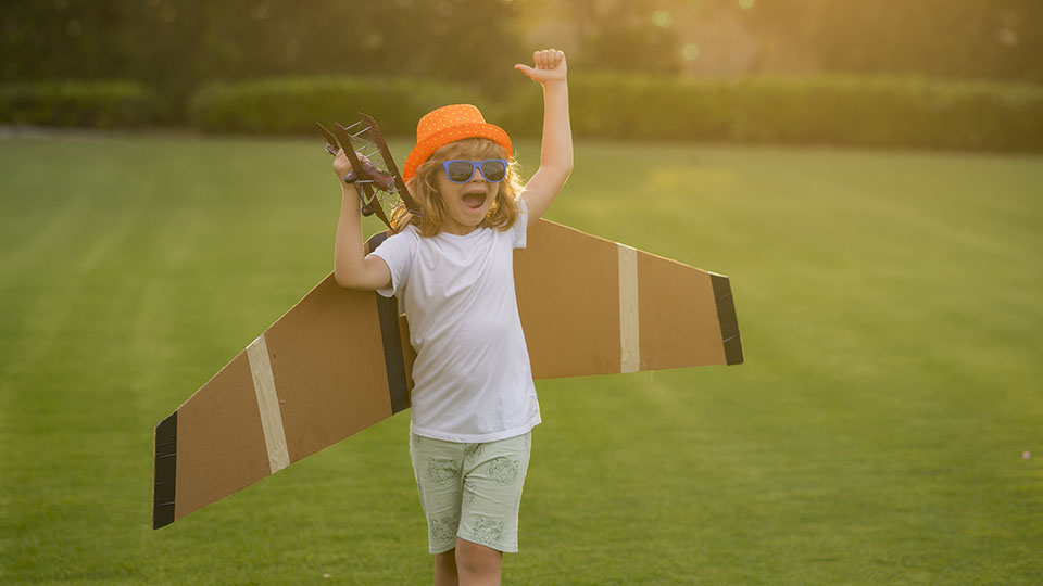 Kinderprogramm Herbst: Junge, der mit gebastelten Flugzeug-Flügeln über Wiese läuft