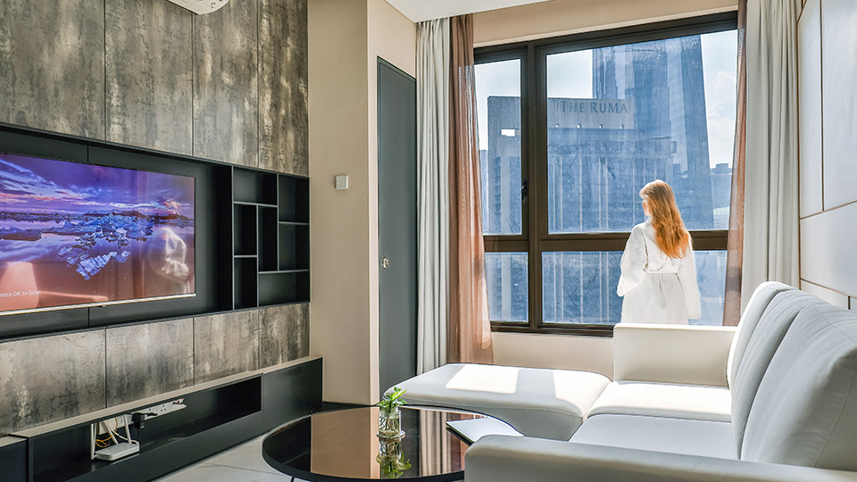 Modernes Hotelzimmer mit großem TV und Entertainment, eine Frau im Bademantel blickt aus dem Fenster