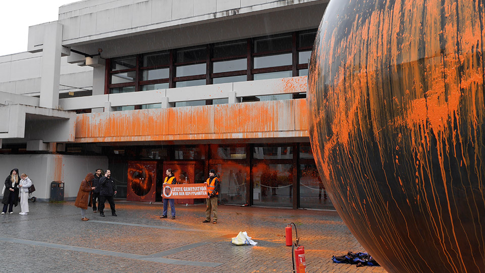 Uni Regensburg vor dem Audimax: Der Eingang und die berühmte Metallkugel sind von Protestierenden der Letzten Generation orange besprüht worden