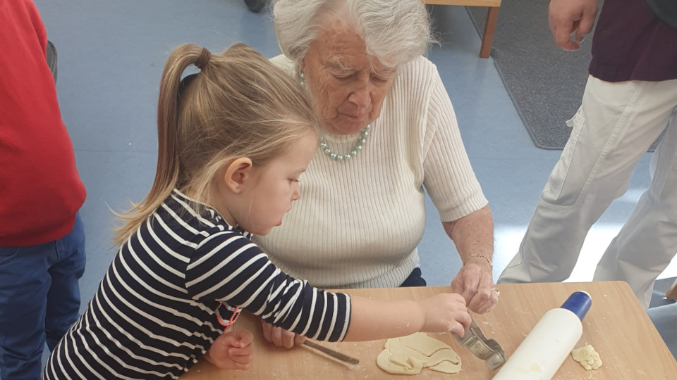Ein Kind backt mit einer alten Dame Plaetzchen