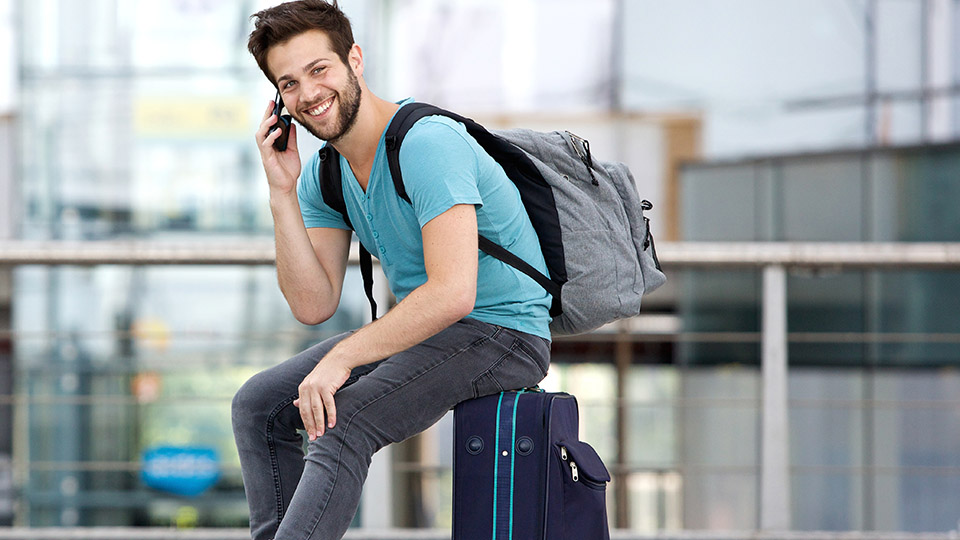 Auslandsreisen: Mann, der am Flughafen ist und mit dem Handy telefoniert