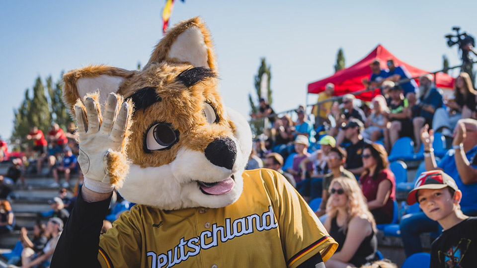Junioren Baseball EM in Regensburg: Fuchs-Maskottchen mit Deutschland-Oberteil winkt, dahinter jubelnde Zuschauer
