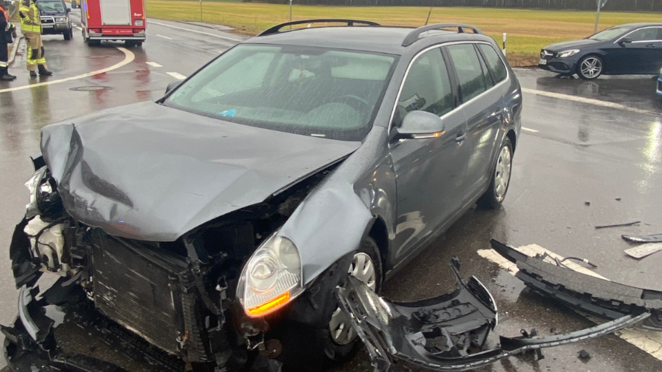 Stark beschädigtes Auto nach Unfall, Feuerwehr im Hintergrund.