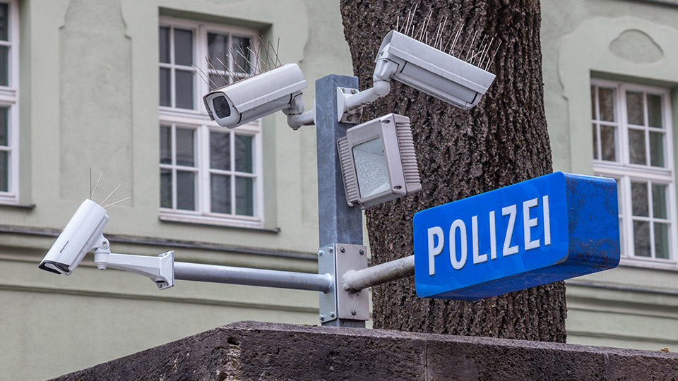 Symbolbild: Überwachungskamera der Polizei mit Polizei-Schild im Vordergrund.