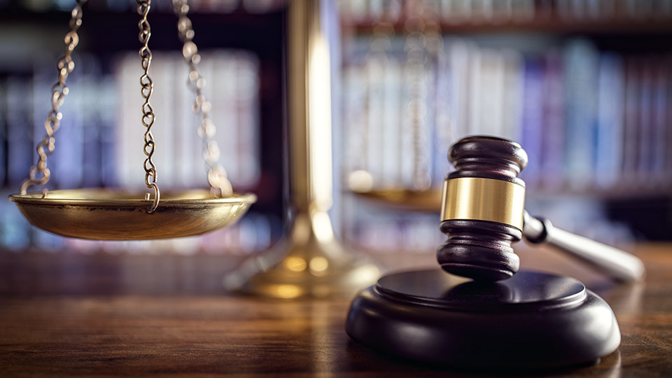 Symbolbild: Richterhammer, Justizwaage und Gesetzesbücher im Gerichtssaal