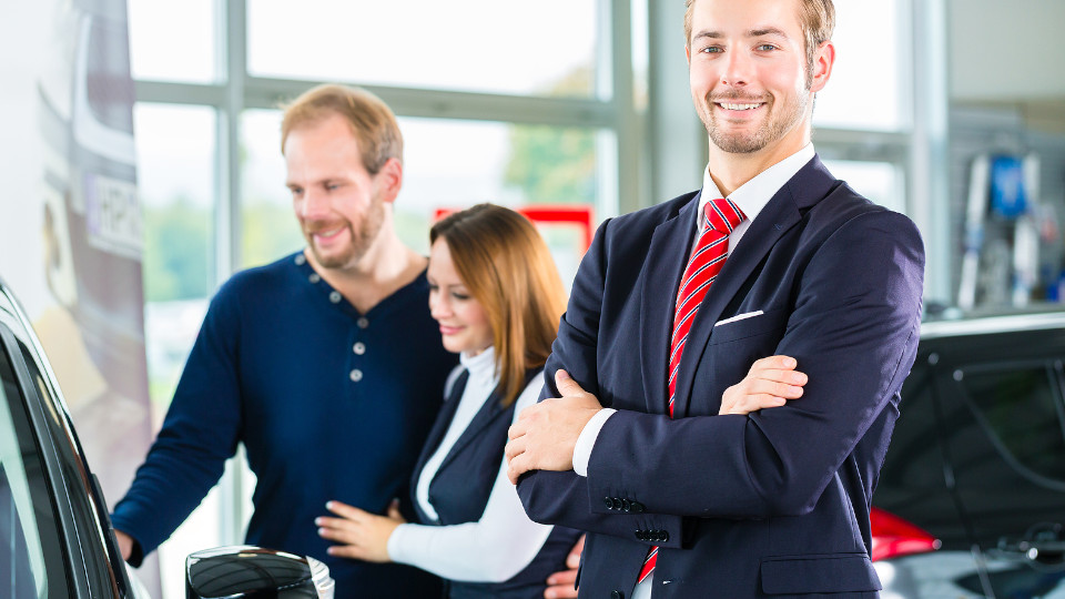 Symbolbild: Pärchen sieht sich ein Auto an, Verkäufer steht daneben