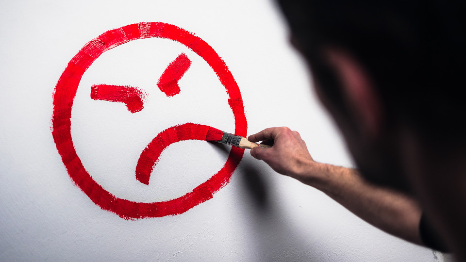 Symbolbild: Maler malt bösen Smiley in rot an die Wand