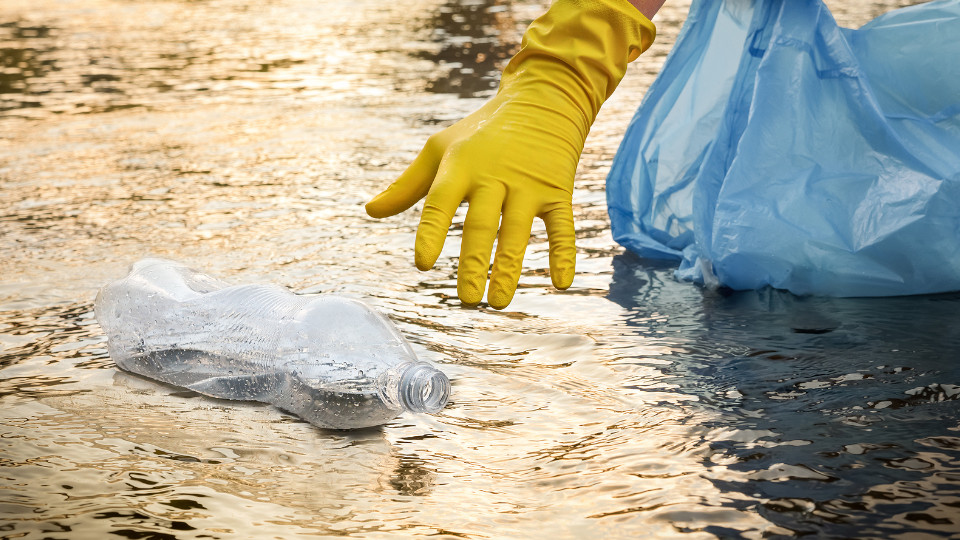 Symbolbild: Plastikflasche im Fluss wird aufgehoben