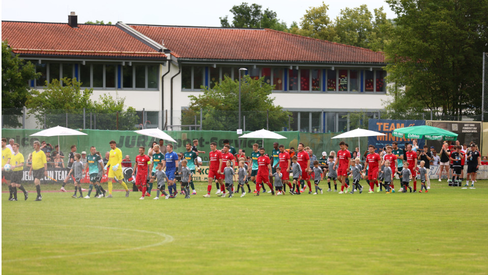 SSV Jahn-Spieler laufen mit Kindern an der Hand auf einem Fußballfeld
