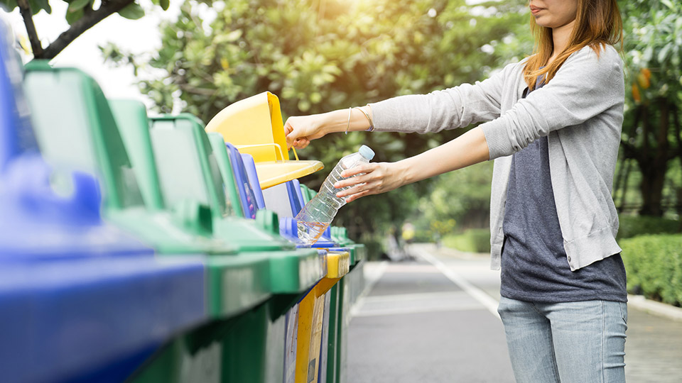 Frau wirft Plastikflasche in die Gelbe Tonne