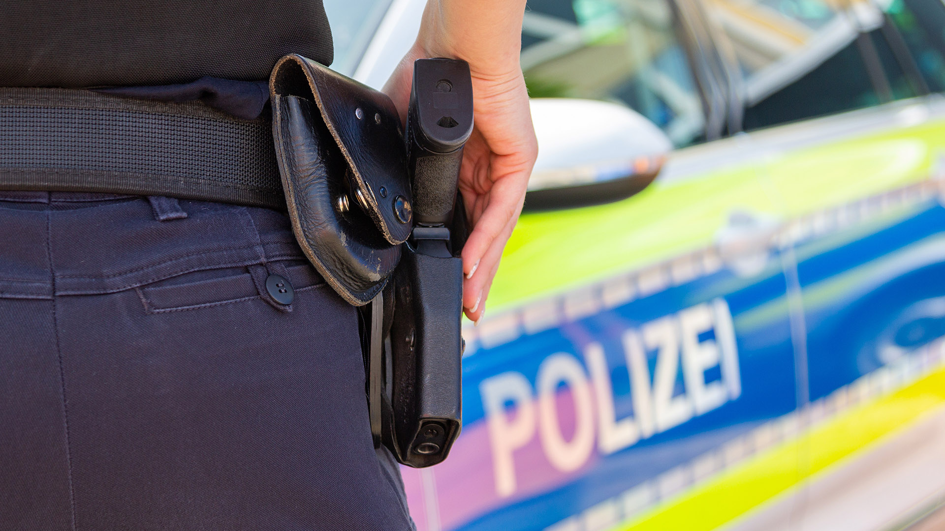 Streifenwagen der Polizei, Polizistin mit der Hand an der Dienstwaffe im Vordergrund