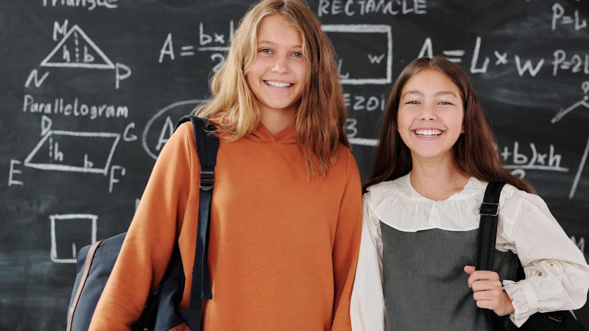 Zwei Mädchen, die lächelnd vor einer Tafel mit mathematischen Formeln stehen.