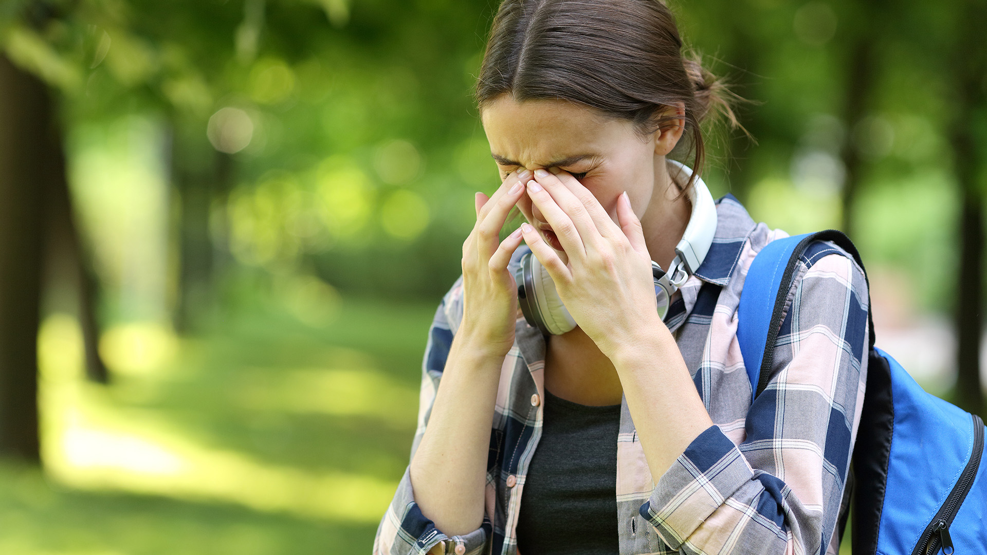 Pollenallergie: Frau im Wald juckt sich die gereizten Augen.