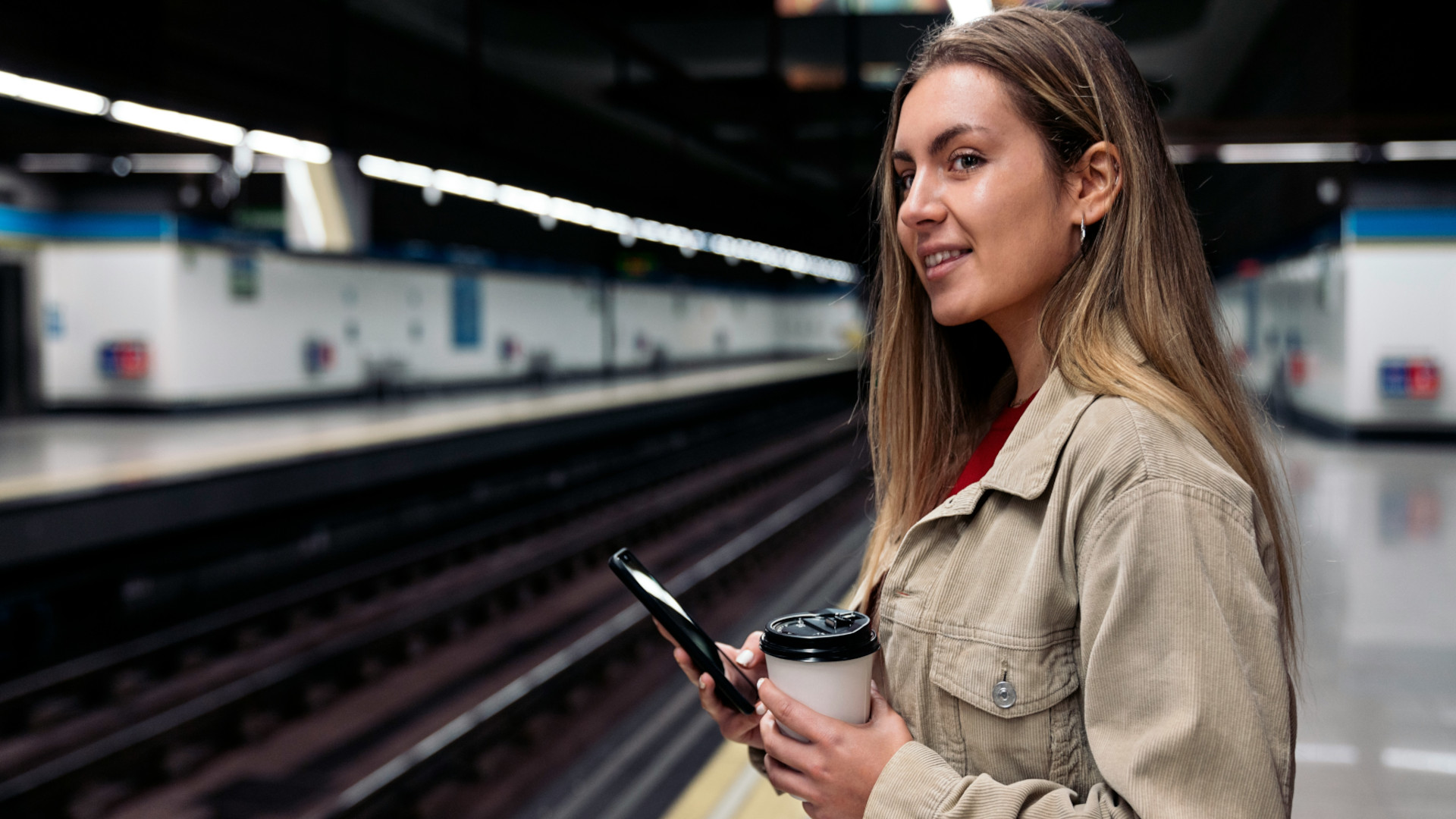 Eine junge Frau am Bahnhof mit dem Handy in der Hand