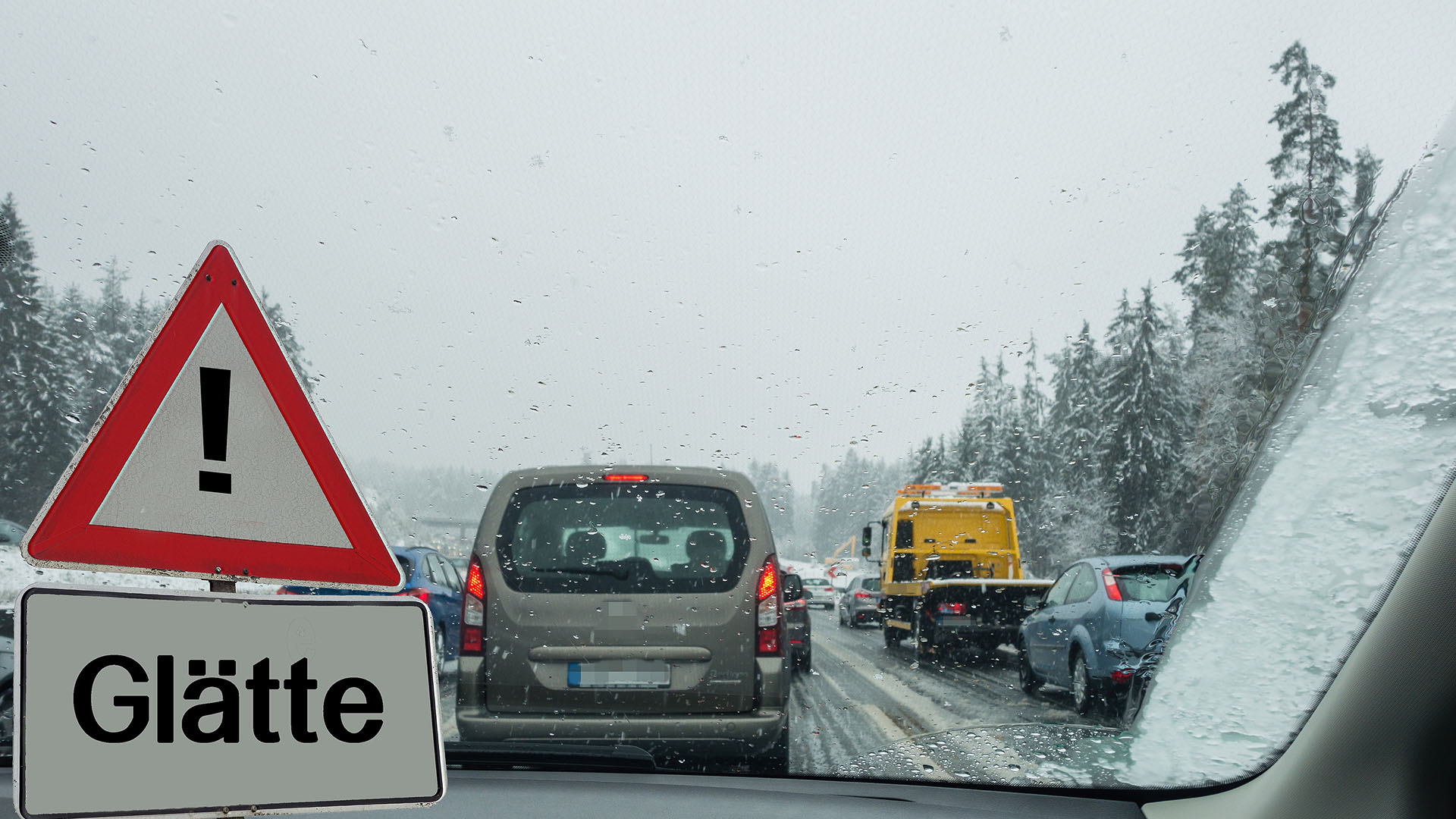 Schild mit Glättewarnung, dahinter ein Verkehrsstau