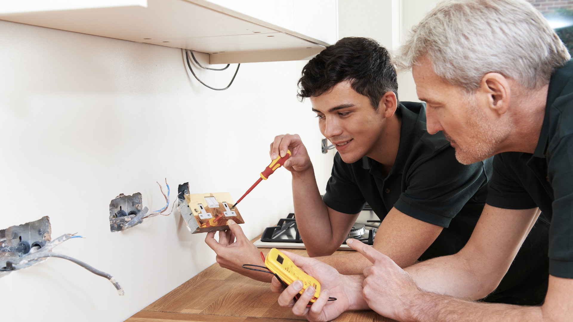 Elektriker arbeitet mit seinem Azubi an einer Steckdose